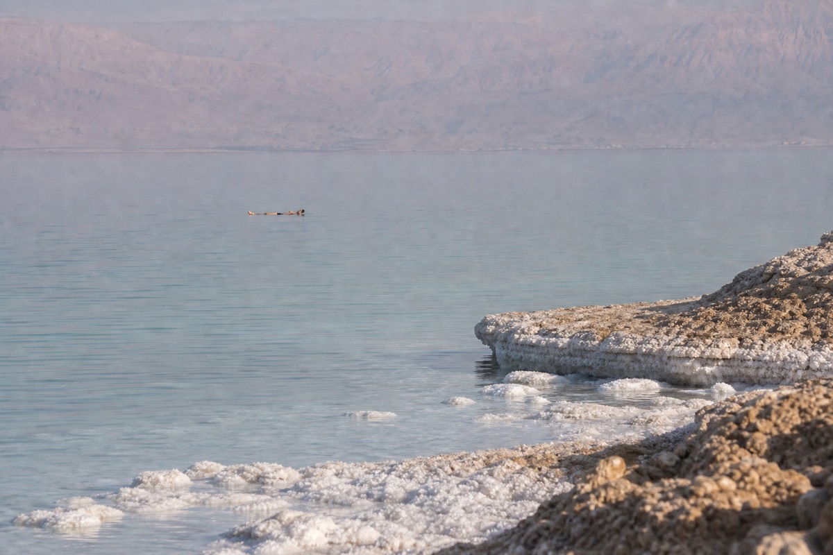 A visitor floating on their back in the Dead Sea with mountains visible across the water
