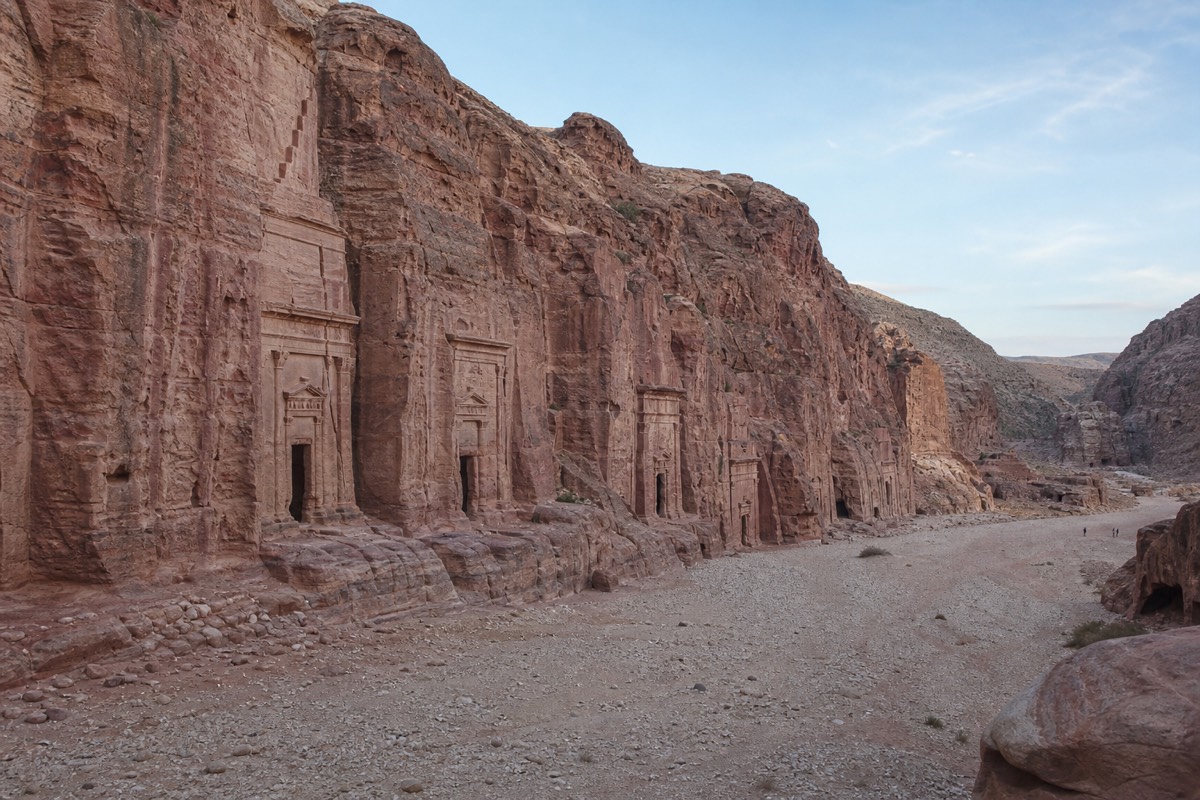 A traveler pausing on a quiet trail above Petra's main basin with rock-cut tombs visible below