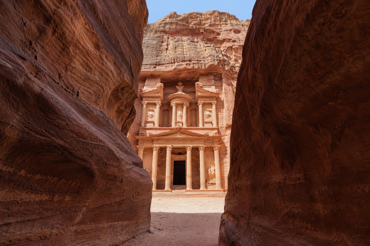 A lone traveler standing at the mouth of the Siq looking toward the Treasury carved into rose-red rock at Petra