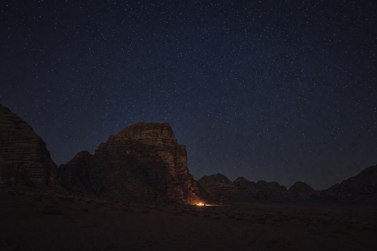 A lit desert camp tent under a star-filled night sky in Wadi Rum