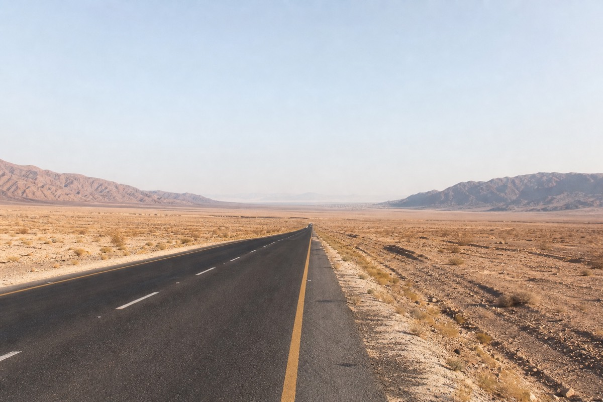 A desert highway leading toward a Jordanian border-crossing checkpoint near the Dead Sea