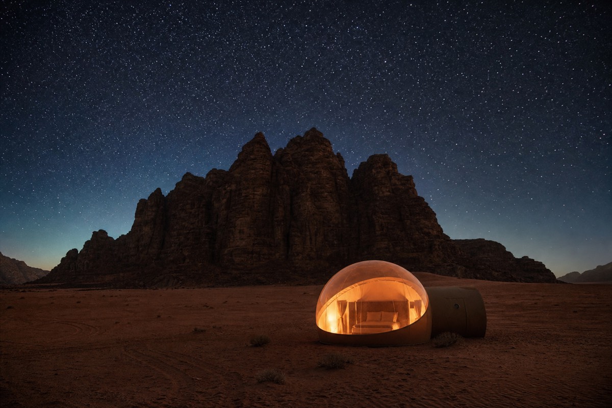A transparent bubble tent glowing at night under a star-filled sky in the Wadi Rum desert