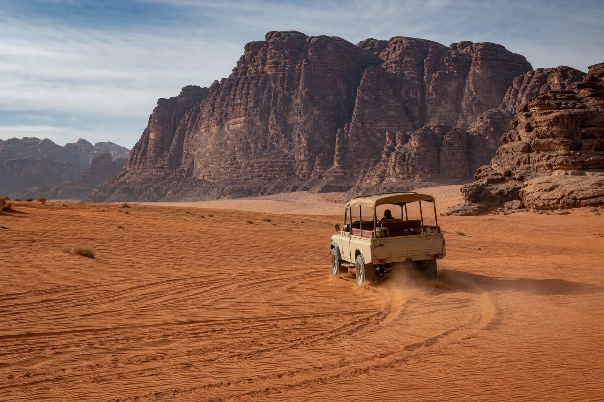 A 4x4 pickup truck kicking up red sand dust in front of towering sandstone cliffs in Wadi Rum desert, Jordan